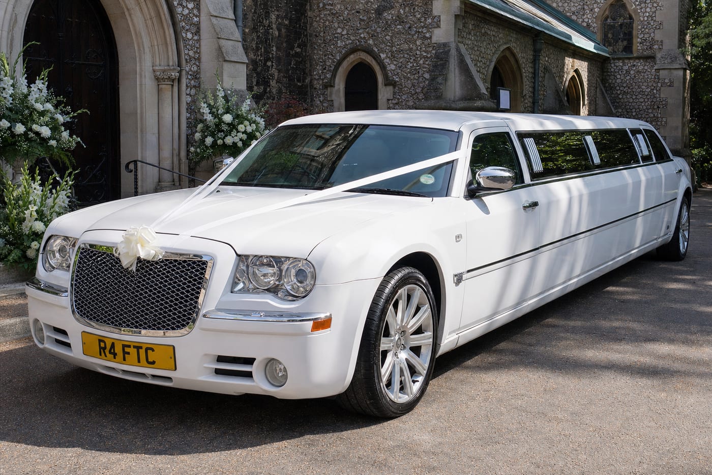 White Chrysler Baby Bentley wedding limousine with ribbons outside a UK church